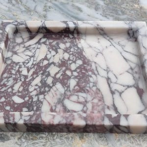May include: A square tray crafted from polished stone featuring a distinct brecciated pattern with deep burgundy and creamy white veining. The tray has a smooth, flat base and raised edges, showcasing a natural, high-contrast marbled texture.