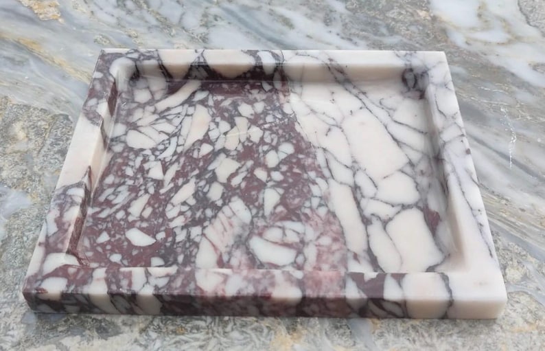 May include: A square tray crafted from polished stone featuring a distinct brecciated pattern with deep burgundy and creamy white veining. The tray has a smooth, flat base and raised edges, showcasing a natural, high-contrast marbled texture.