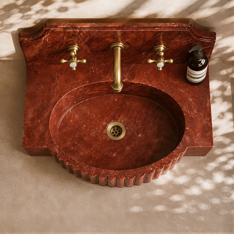 a red marble sink with a gold faucet, placed on a beige tiled floor. There is a bottle of soap next to the sink.