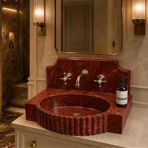 a bathroom with a red marble sink and a gold faucet, along with a mirror above it. There is also a bottle of soap placed on the sink.