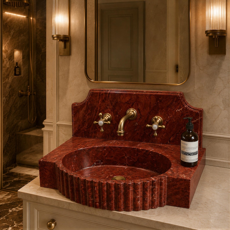 a bathroom with a red marble sink and a gold faucet, along with a mirror above it. There is also a bottle of soap placed on the sink.