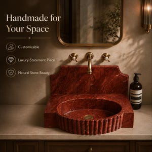 a luxurious bathroom sink made of red marble, with a gold faucet and a mirror above it. The sink is described as handcrafted and customizable, with a statement piece of luxury, natural stone beauty, and a natural stone statement piece.