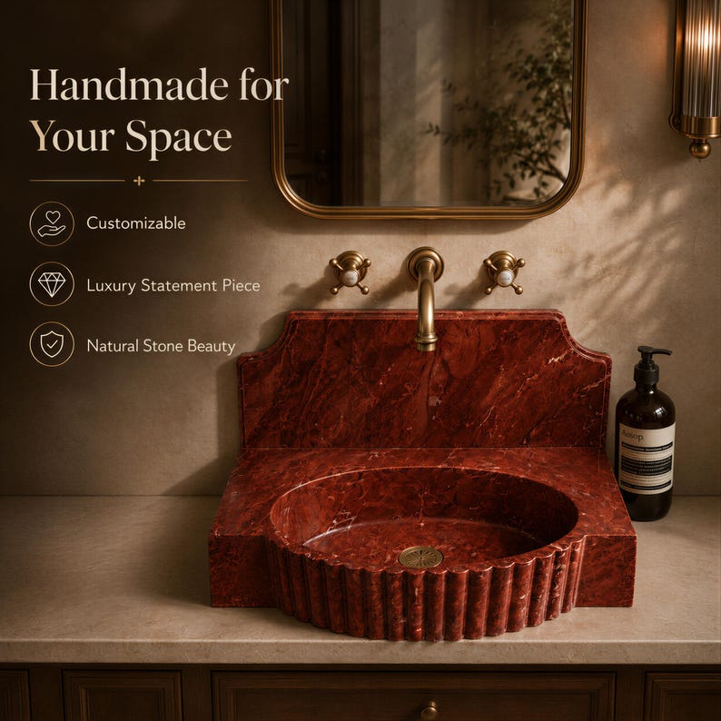 a luxurious bathroom sink made of red marble, with a gold faucet and a mirror above it. The sink is described as handcrafted and customizable, with a statement piece of luxury, natural stone beauty, and a natural stone statement piece.