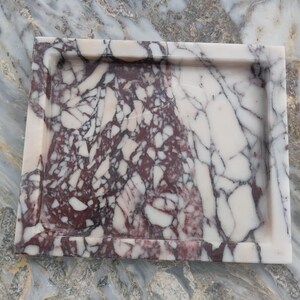 May include: A square marble tray featuring a distinct color split, with one half displaying a deep burgundy and white brecciated pattern and the other half showing a creamy white surface with dark grey veining throughout the stone material.