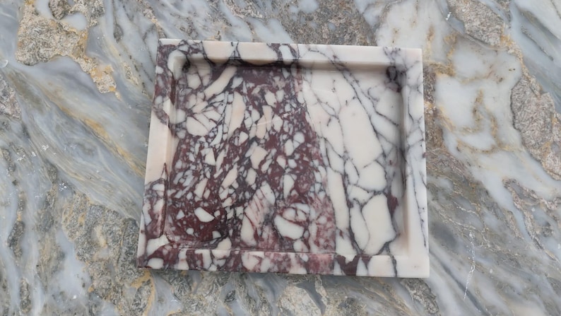 May include: A square marble tray featuring a distinct color split, with one half displaying a deep burgundy and white brecciated pattern and the other half showing a creamy white surface with dark grey veining throughout the stone material.