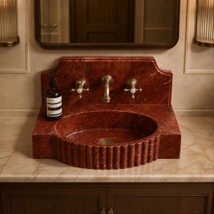 a bathroom sink with a red marble basin, a gold faucet, and a bottle of soap on the countertop.