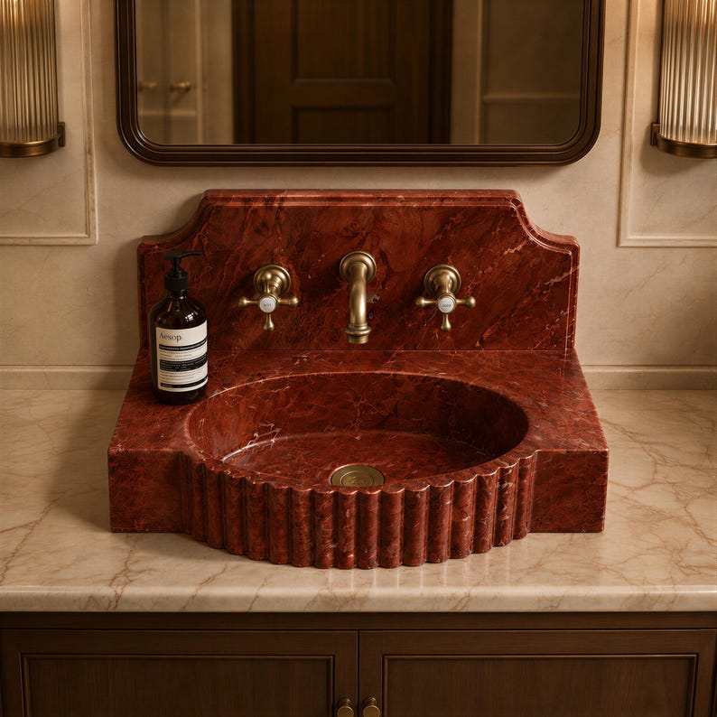 a bathroom sink with a red marble basin, a gold faucet, and a bottle of soap on the countertop.
