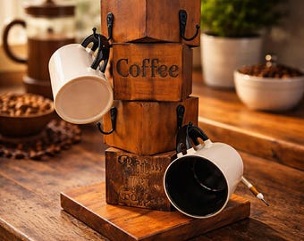 May include: A wooden coffee mug holder with four stacked, square blocks. The blocks are stained brown and have black hooks for hanging mugs. The word "Coffee" is carved into one block. Two white mugs with black handles hang from the hooks.