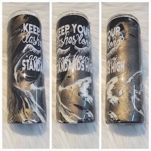May include: A black and gold tumbler with a white marble design. The tumbler has the text "Keep your lashes long and your standards high" written on it.