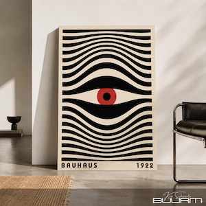 Pode incluir: Uma impressão de arte de parede retangular com fundo creme e linhas onduladas pretas horizontais que convergem para um círculo vermelho central com uma pupila preta. O texto BAUHAUS está impresso em preto no canto inferior esquerdo e 1922 à direita.