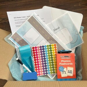 May include: A cardboard box filled with educational materials. Includes flashcards, stickers, a toy car, and printed sheets with road and water droplet designs. The box also contains a blue eraser, a black marker, and blue plastic sleeves.