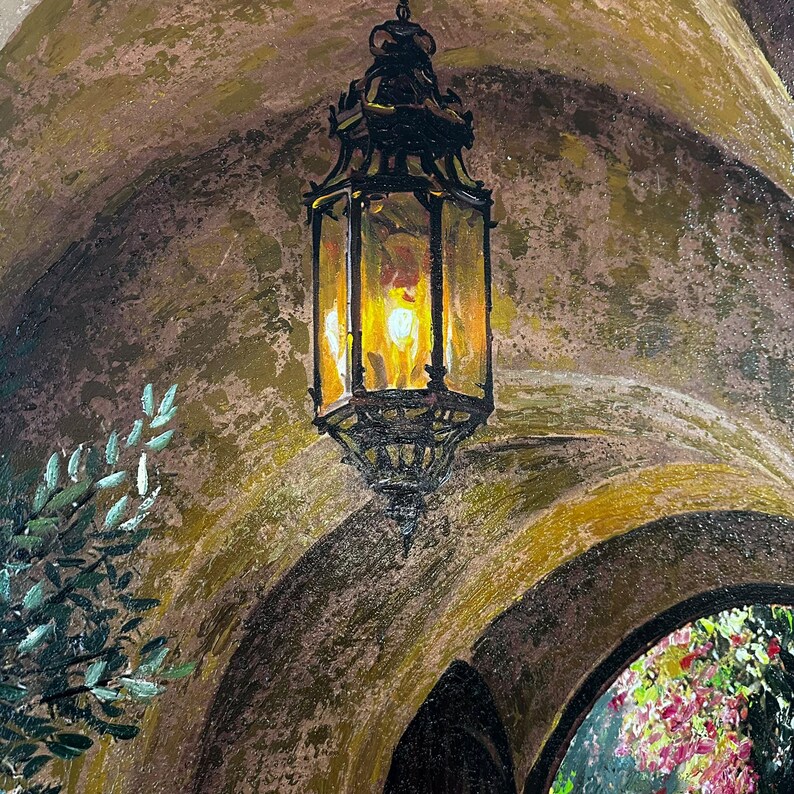 May include: An oil painting depicting a dark metal hanging lantern with a warm yellow glow inside, suspended within a textured, arched stone-colored entryway. Green foliage is visible on the left, and colorful flowers appear in the distance.