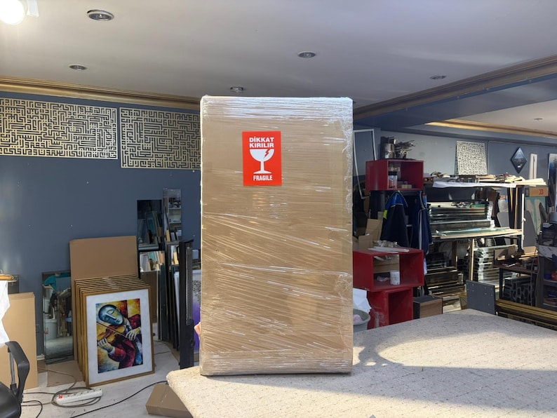 May include: A large rectangular cardboard box wrapped in clear plastic film. A bright red rectangular sticker is centered on the front, featuring a white wine glass icon and the text DIKKAT KIRILIR FRAGILE in white capital letters.