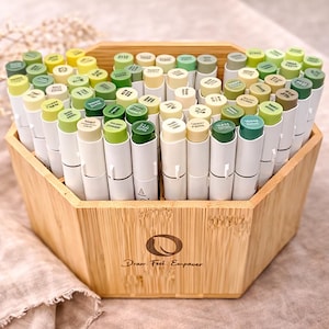 May include: A selection of green and yellow art markers, displayed in a hexagonal bamboo box. The markers have white barrels and colour-coded caps. The box has the text "Draw. Feel. Empower."
