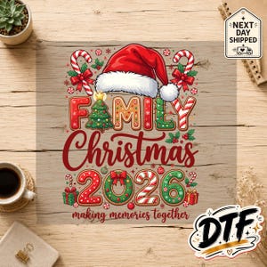以下が含まれることがあります： 赤いサンタの帽子と「Family Christmas 2026 making memories together」という文字が描かれたグラフィック転写シート。ジンジャーブレッド風の文字、キャンディケイン、クリスマスツリー、リース、赤と緑のギフトボックスがデザインされています。