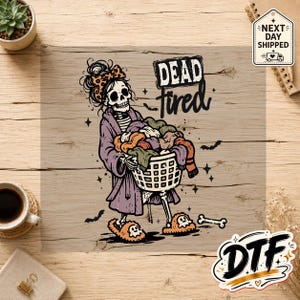 May include: A graphic print featuring a skeleton wearing a purple robe, a leopard print headband, and skull slippers, carrying a laundry basket filled with colorful clothing. The text reads "DEAD tired" in a bold, stylized black font.