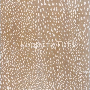 May include: A rectangular rug with a tan background and a pattern of white, irregular spots. The rug's design resembles animal hide. The text "LoopifyTuffs" is printed in white across the center of the rug.