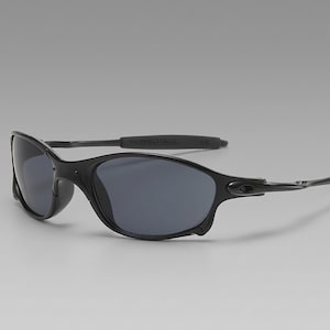 May include: Black sunglasses with dark gray lenses. The sunglasses have a sleek, curved frame and arms. The lenses are oval-shaped and provide full coverage. The arms have a rubberized grip for comfort and stability. The sunglasses are designed for outdoor activities.