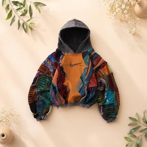 May include: A patchwork hoodie with a gray hood and a brown front panel featuring the Nike logo and text. The sleeves are made of colorful, textured fabric patches in various colors, including blue, orange, and green.
