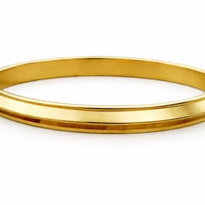 Puede incluir: Un brazalete dorado con una banda plana y ancha y un borde ligeramente elevado. El brazalete tiene un acabado liso y pulido y un diseño simple y elegante. La joya es adecuada para el uso diario.