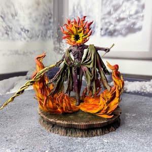 May include: A detailed figurine of a humanoid figure with a fiery head and flames surrounding its base. The figure is painted in shades of purple, orange, and yellow, with a staff in one hand and a flowing cape. The base is a textured, wooden-like platform.