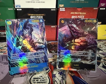 May include: Two One Piece trading cards displayed on stands. The left card features Rocks D. Xebec with a cost of 10 and 12000 power. The right card features Loki with a cost of 6 and 8000 power. Both cards have holographic foil details.