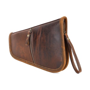 Può includere: Una custodia in pelle marrone con chiusura a zip e cinturino da polso. La custodia ha una finitura invecchiata, con variazioni di colore dal marrone chiaro allo scuro. La cerniera e i dettagli sono color bronzo.