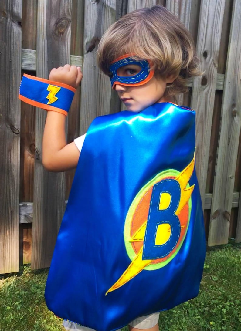 Blue satin cape, mask, and cuffs. Mask and cuffs are made from felt and are one size fits all. They are machine washable and secured with velcro for an easy on and off.