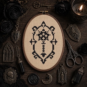 May include: An oval wooden embroidery hoop containing a beige fabric panel with a black cross-stitch design featuring a central geometric emblem and a vertical line of small squares, surrounded by various dark metal accessories and black roses.