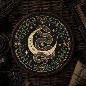 May include: A circular cross-stitch design in a wooden frame, depicting a snake wrapped around a crescent moon. The embroidery uses black, brown, and green threads, with floral and star motifs. The overall style suggests a gothic or mystical theme.