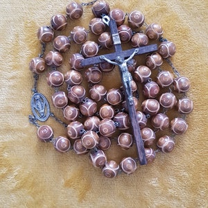 May include: A brown wooden rosary with a silver crucifix and a silver charm of the Virgin Mary. The beads are round and have a white design.
