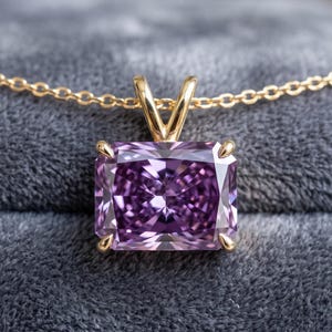 Puede incluir: Un colgante con una piedra preciosa morada de corte radiante montada en cuatro garras de oro, suspendido de una fina cadena de oro. La piedra rectangular presenta superficies facetadas que captan la luz, sujeta por una anilla de oro.
