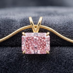 May include: A rectangular pink gemstone pendant set in a gold four-prong mounting. The pendant is attached to a gold snake chain necklace. The gemstone features a faceted cut that reflects light, creating a brilliant appearance across the surface.