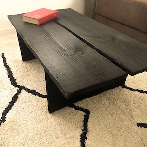 Pode incluir: Uma mesa de centro de madeira preta com um tampo retangular e um design simples e moderno. Um livro vermelho repousa sobre a superfície da mesa. A mesa tem aproximadamente 122 cm de comprimento e 51 cm de largura.