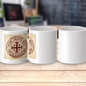 May include: White ceramic mug with a handle. The mug features a design with a red cross and the words "VIVA CRISTO REY" in a circular emblem. The design is on a tan background. The mug is displayed on a wooden surface.