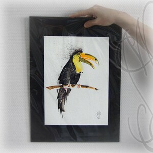 May include: A framed watercolor painting of a toucan bird perched on a branch. The bird has black feathers, a yellow chest, and a large yellow and orange beak. The artwork is in a black frame.