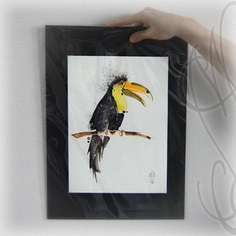 May include: A framed watercolor painting of a toucan bird perched on a branch. The bird has black feathers, a yellow chest, and a large yellow and orange beak. The artwork is in a black frame.