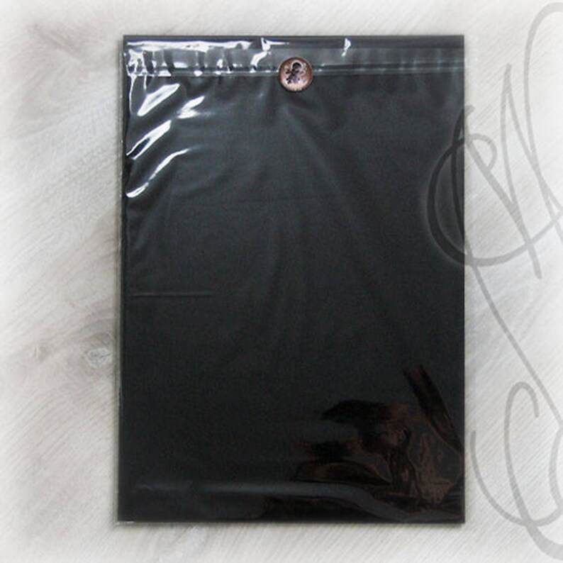 May include: A black, rectangular package sealed in clear plastic. A decorative button with a floral design secures the top. The package is likely for shipping or presentation of an item.