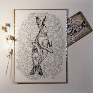 K&ouml;nnte beinhalten: Schwarz-Wei&szlig;-Illustration eines Hasen, mit detailliertem Zeichenstil. Der Hase ist kopf&uuml;ber, vor einem wirbelnden Hintergrund. Eine kleinere Karte mit einem &auml;hnlichen Hasen-Design ist sichtbar.
