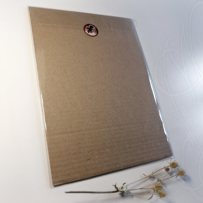 K&ouml;nnte beinhalten: Ein brauner Karton-Kunstdruck, versiegelt in klarem Kunststoff, mit einem kleinen runden Aufkleber in der oberen rechten Ecke. Der Druck wird auf einer wei&szlig;en Oberfl&auml;che mit getrockneten Blumen im Vordergrund pr&auml;sentiert.