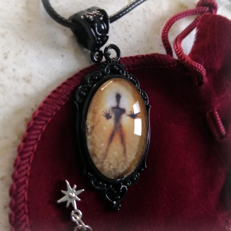 Puede incluir: Collar con colgante negro con un dije ovalado que presenta una figura de silueta sobre un fondo dorado c&aacute;lido. El colgante est&aacute; enmarcado en un marco decorativo de metal negro y cuelga de un cord&oacute;n negro. Un peque&ntilde;o dije de estrella cuelga debajo.