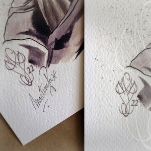 May include: Two watercolor paintings on textured paper. The left painting features a dark, abstract figure with a signature and the date '22'. The right painting shows a similar figure with a lighter color palette and a faint design.