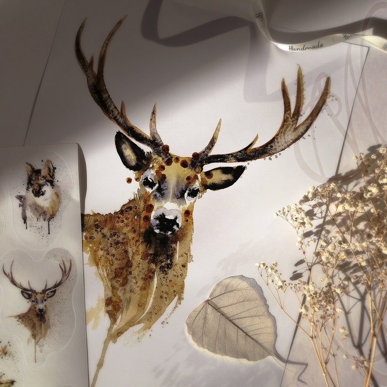 May include: A watercolour painting of a deer with large antlers, in brown and tan tones. The image includes sticker sheets with animal illustrations and a leaf. A ribbon with the word "Handmade" is visible.