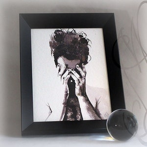 K&ouml;nnte beinhalten: Schwarz gerahmter Kunstdruck mit einem Aquarellportr&auml;t in Graustufen, das eine Person mit verdecktem Gesicht zeigt. Eine klare Glaskugel liegt auf einer wei&szlig;en Oberfl&auml;che.