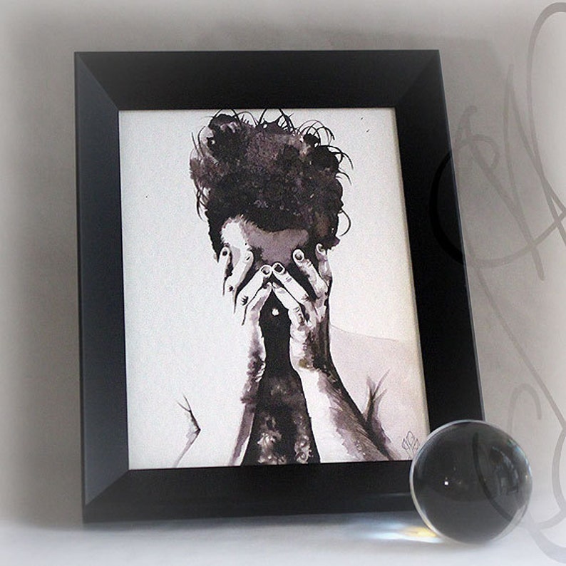 K&ouml;nnte beinhalten: Schwarz gerahmter Kunstdruck mit einem Aquarellportr&auml;t in Graustufen, das eine Person mit verdecktem Gesicht zeigt. Eine klare Glaskugel liegt auf einer wei&szlig;en Oberfl&auml;che.
