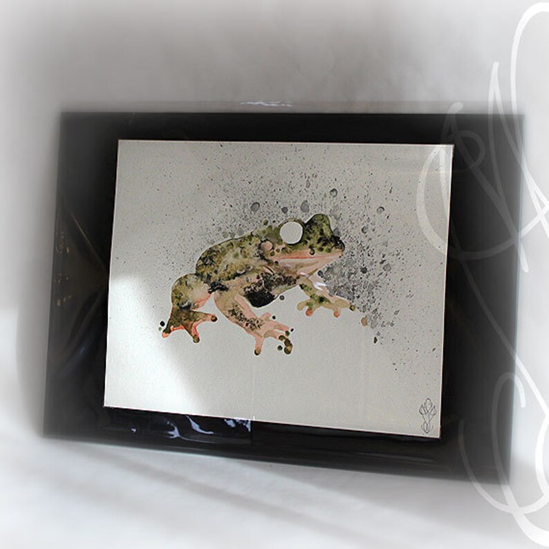 Puede incluir: Obra de arte enmarcada con una ilustraci&oacute;n de una rana. La rana est&aacute; representada en tonos verdes, marrones y negros, con vientre y patas de color rosa claro. El fondo es gris claro con salpicaduras grises m&aacute;s oscuras. El marco es negro.