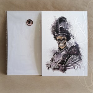 May include: Watercolor print of a skeleton in a feathered hat and armor. The artwork is in shades of black, gray, and gold, with splatters of dark ink. A blank white card is in a clear sleeve, sealed with a copper-colored sticker.