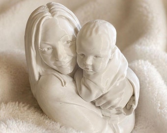 Könnte beinhalten: Eine weiße Skulptur, die eine Mutter mit ihrem Baby zeigt. Die Mutter mit langem Haar lächelt, während sie das Baby im Arm hält. Das Baby ist in ihren Armen geborgen. Die Skulptur steht auf einem weichen, weißen, strukturierten Hintergrund.