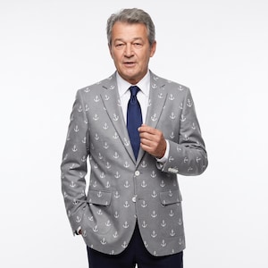 May include: A gray blazer featuring a repeating white anchor pattern, worn with a crisp white collared shirt and a solid navy blue necktie. The blazer includes notched lapels, two front flap pockets, and white buttons on the front and cuffs.
