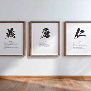 May include: Three framed wall art prints featuring black ink calligraphy characters with small red stamps. Each print includes phonetic text and English definitions below the central character, all encased in light brown wooden frames.